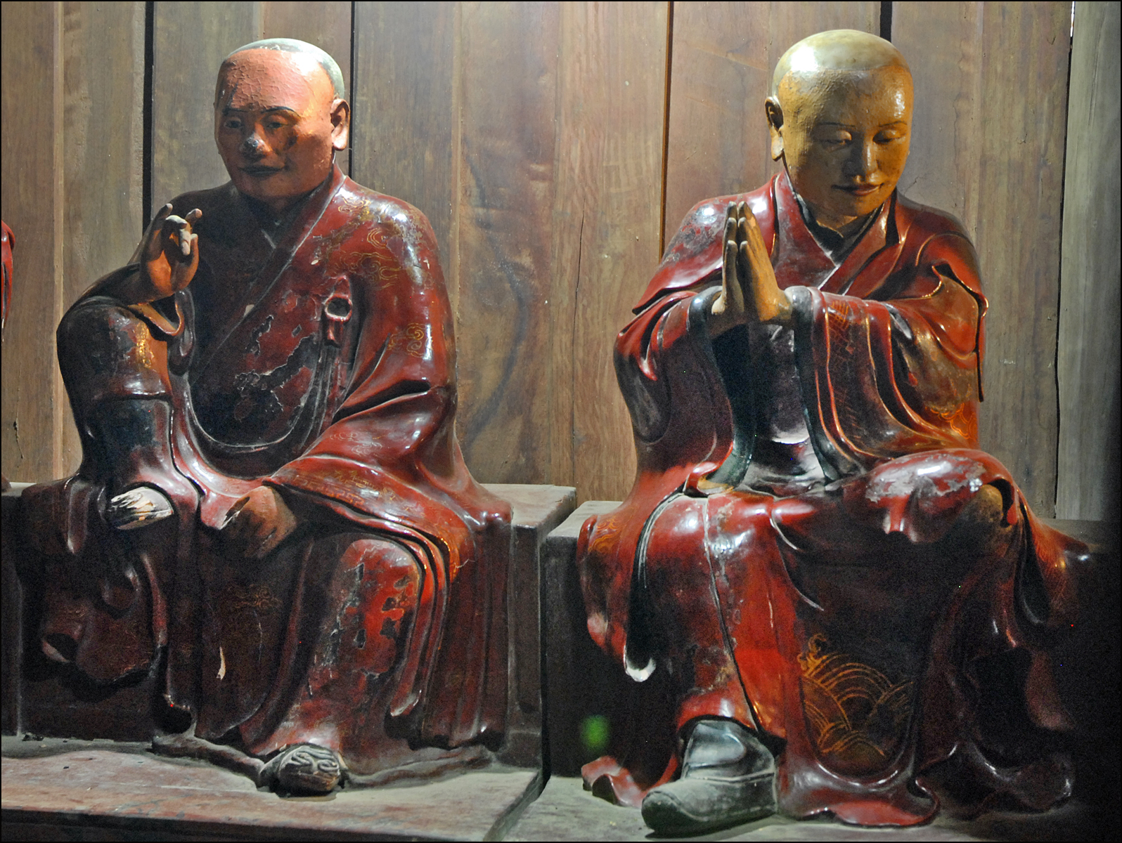 two statues of monks are sitting in front of wooden planks
