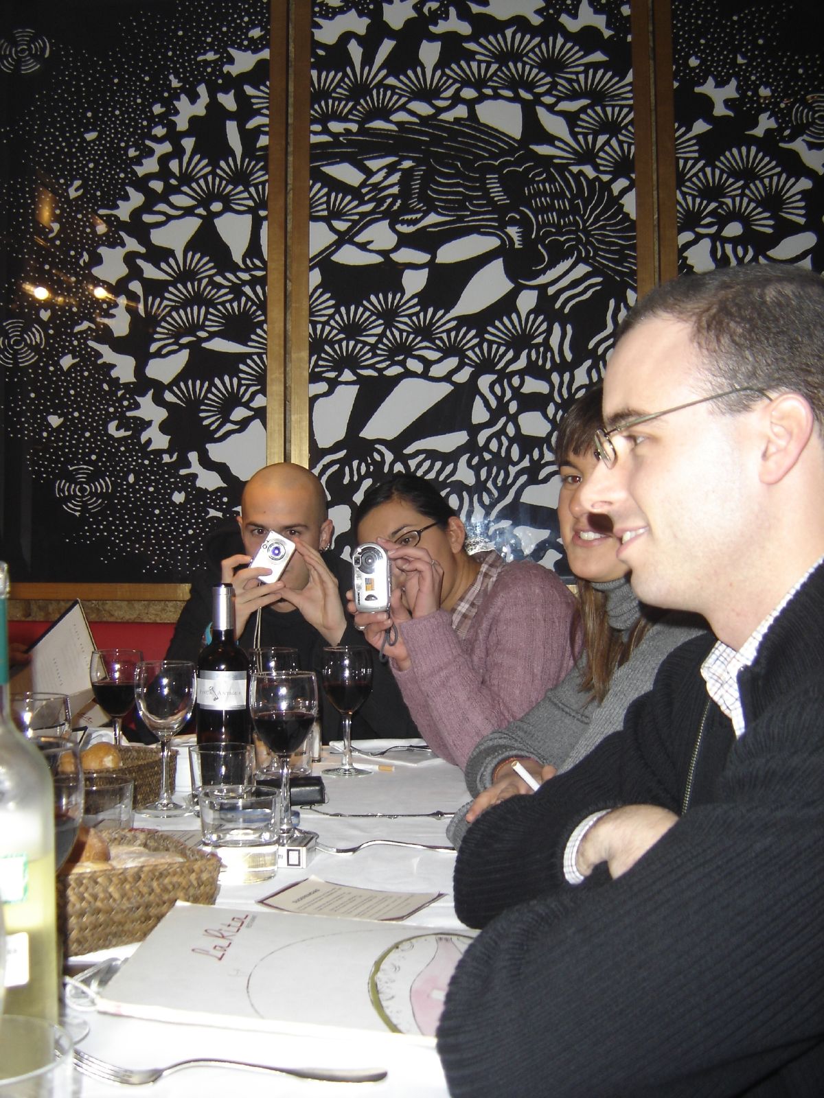 four people at table, one drinking a beverage and the other sitting at a restaurant