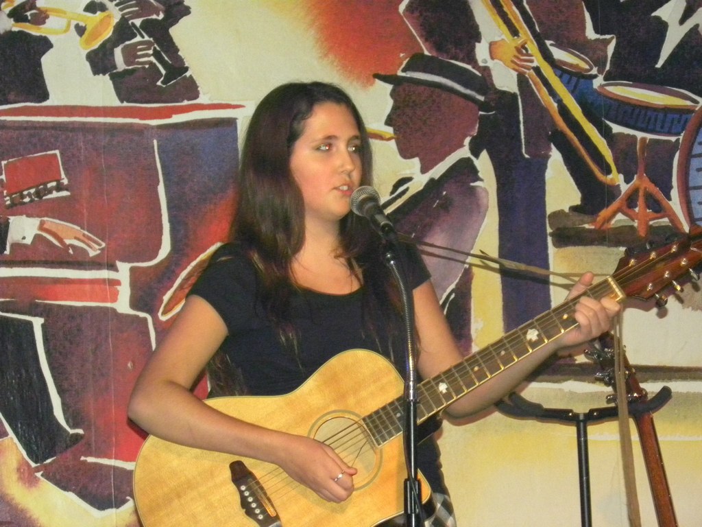 a young woman is playing a guitar while another sings into a microphone