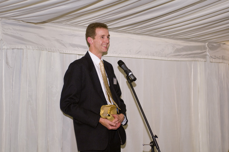 a man standing next to a microphone with a trophy