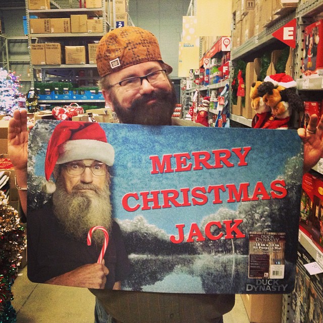 a man in glasses holds a sign with an image of a santa clause holding a candy cane