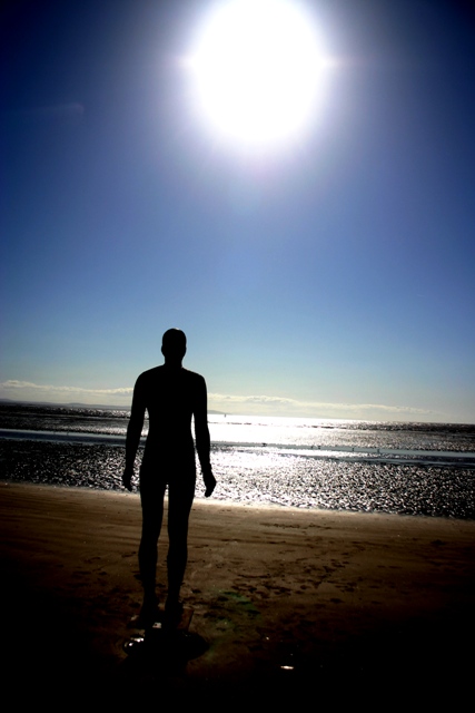 a person stands on the beach looking at the sun