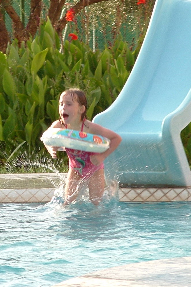 girl swimming in pool near large slide and green bush