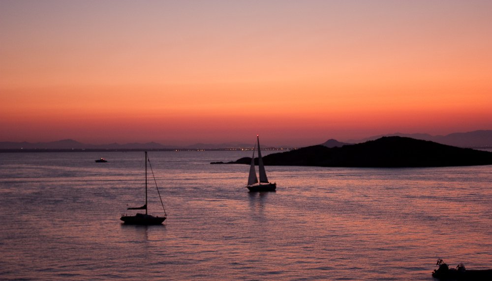 a group of boats in the ocean at sunset