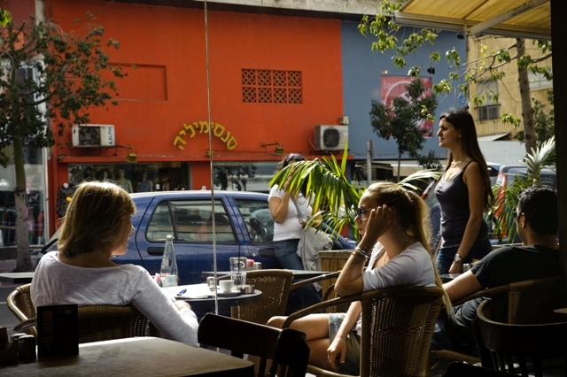 several women sitting at an outdoor cafe with their phones to their ears