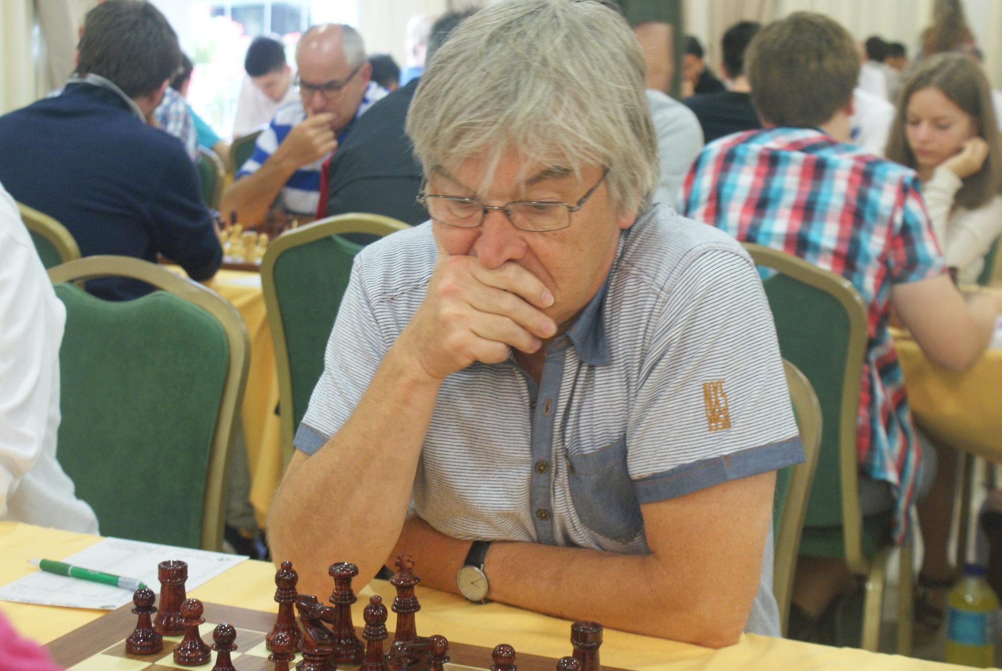 an elderly man looks intently at the chess game