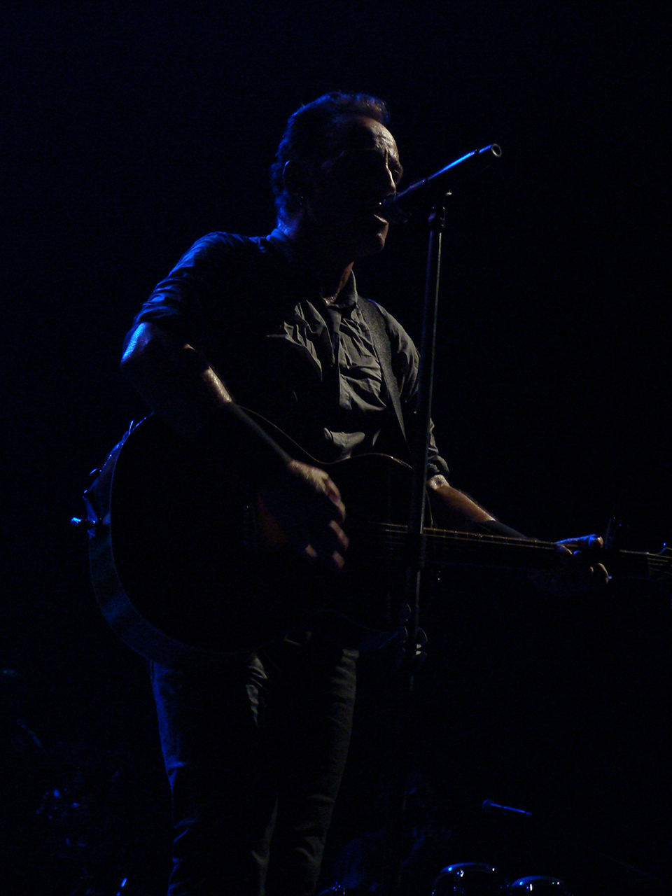 man playing guitar in front of microphone and dark stage