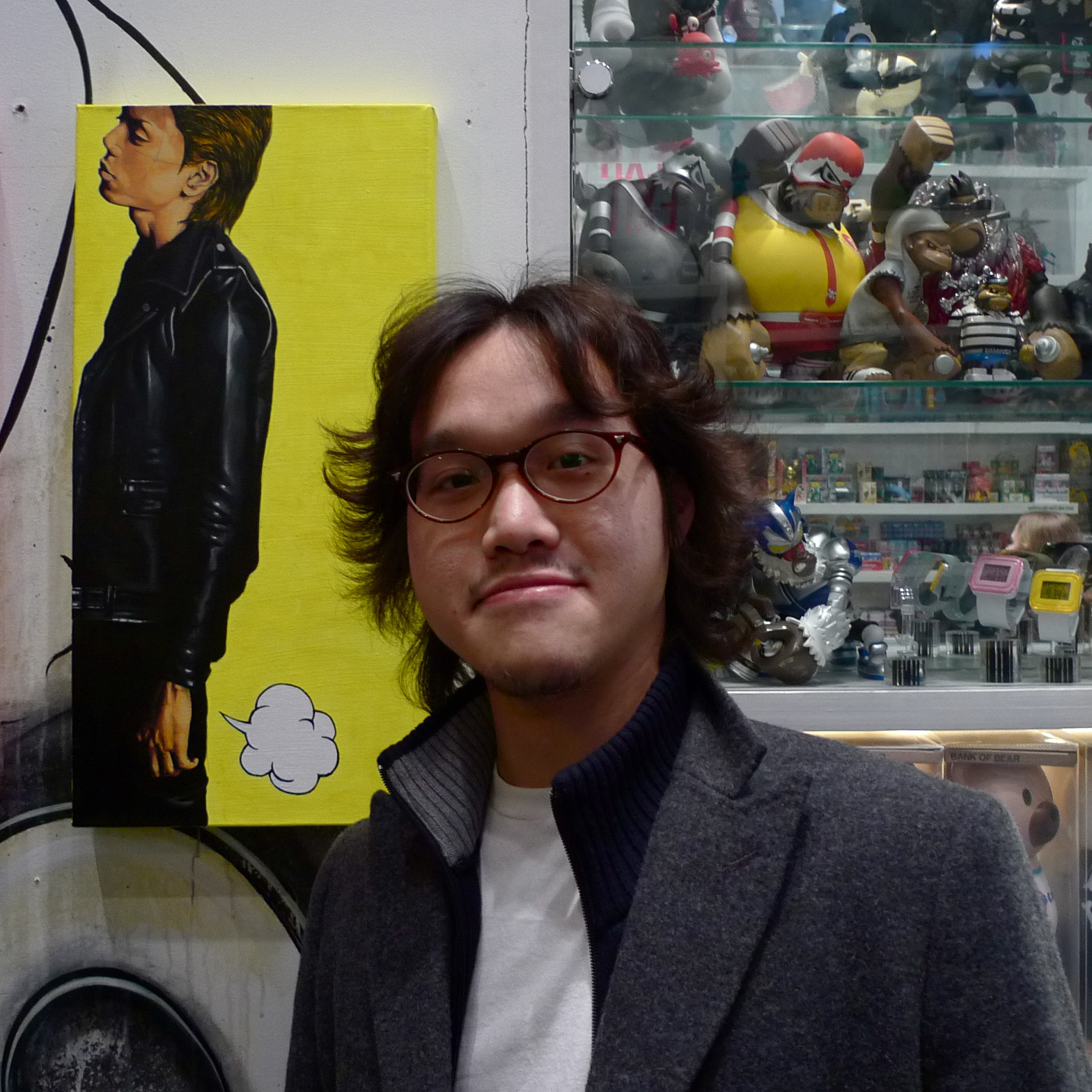 a man wearing glasses standing next to a piece of art