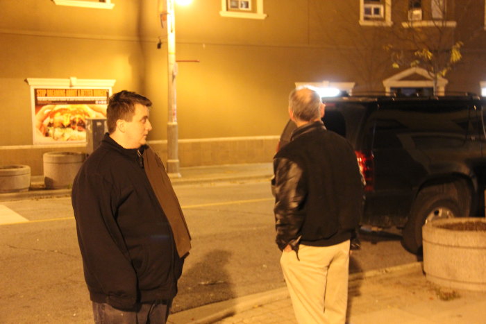 two men standing on a sidewalk next to the street