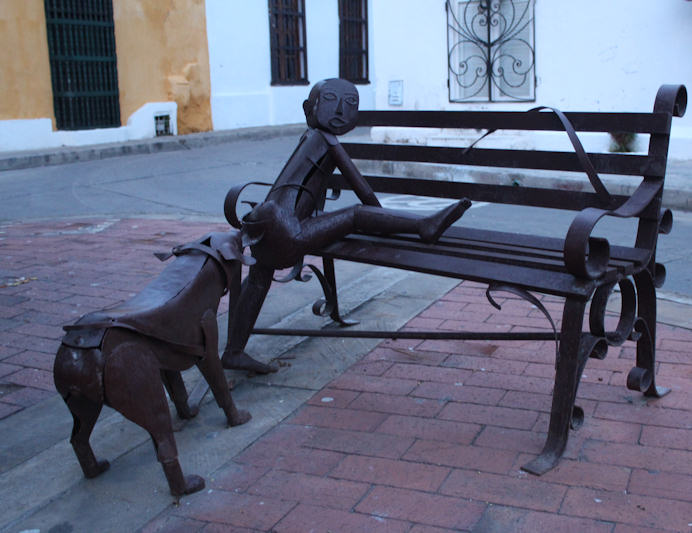 a park bench with metal statues of people and a dog