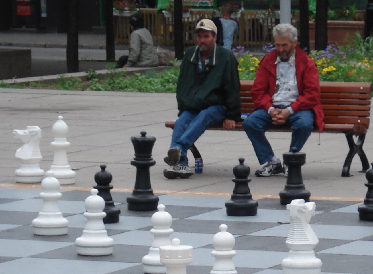 two people are sitting on a bench surrounded by chess pieces