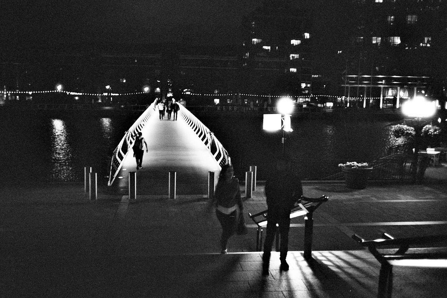 people walking across the bridge at night in black and white