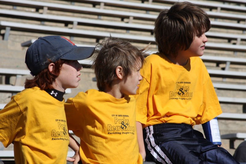 three little boys looking to their left sitting on the bleachers