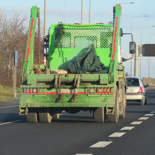 two large green trucks driving on a street