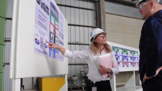a woman points at a poster in a factory