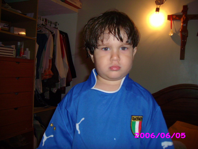 young child dressed in blue with italy badge standing next to messy wardrobe