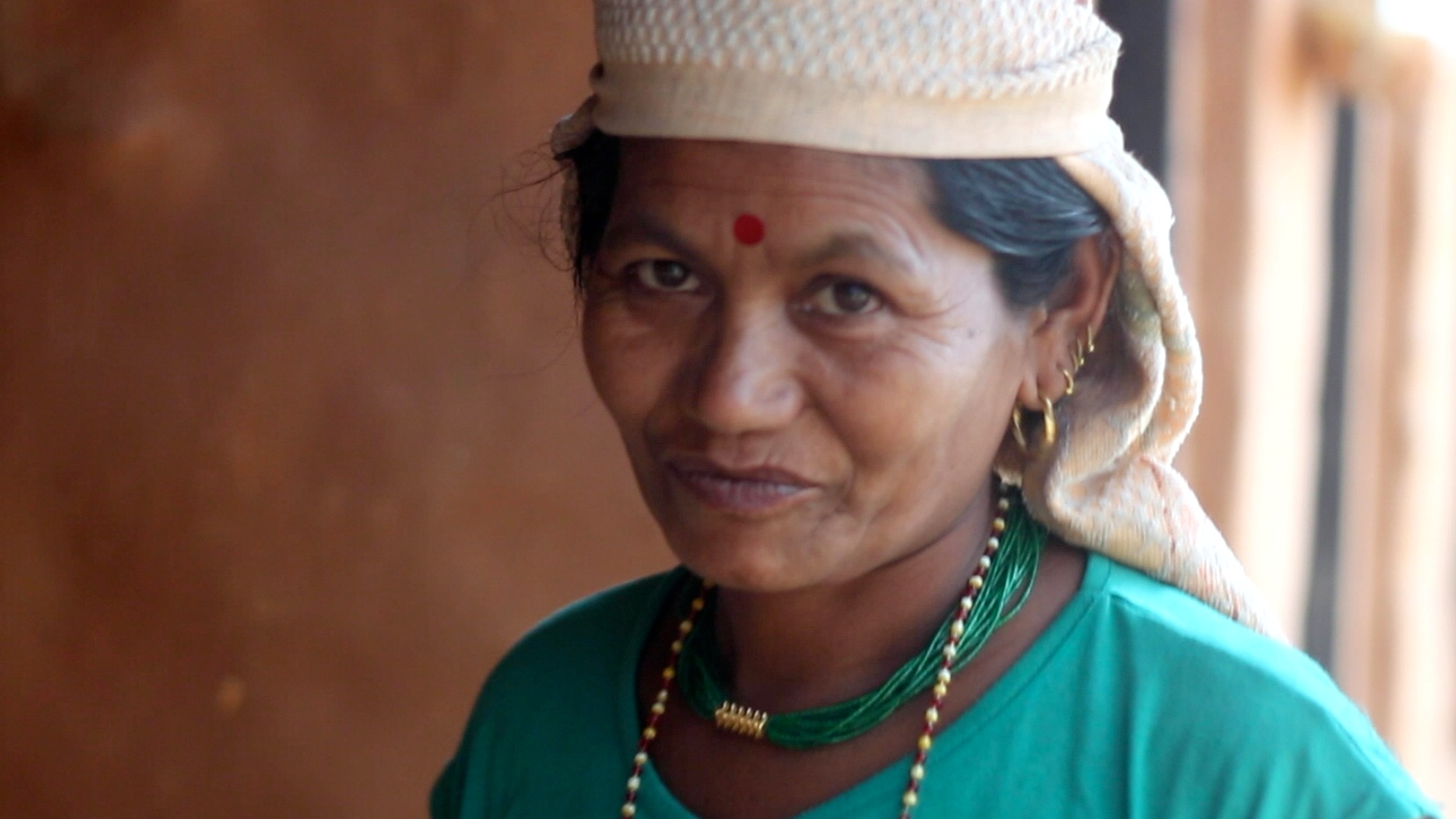 a woman with necklaces on in front of wooden wall