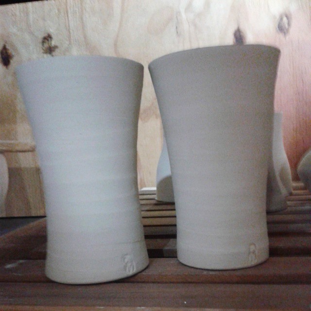 two white vases sit on wooden boards and have holes in the rim