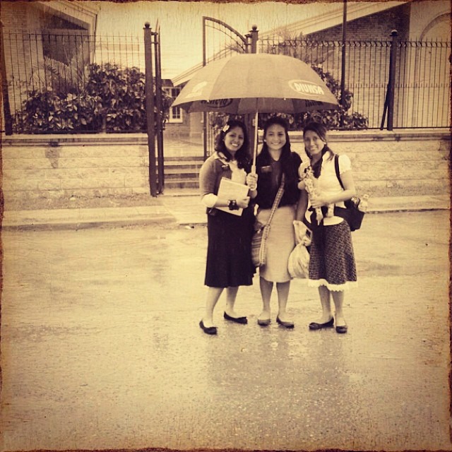 three girls smile as they stand in the rain under an umbrella
