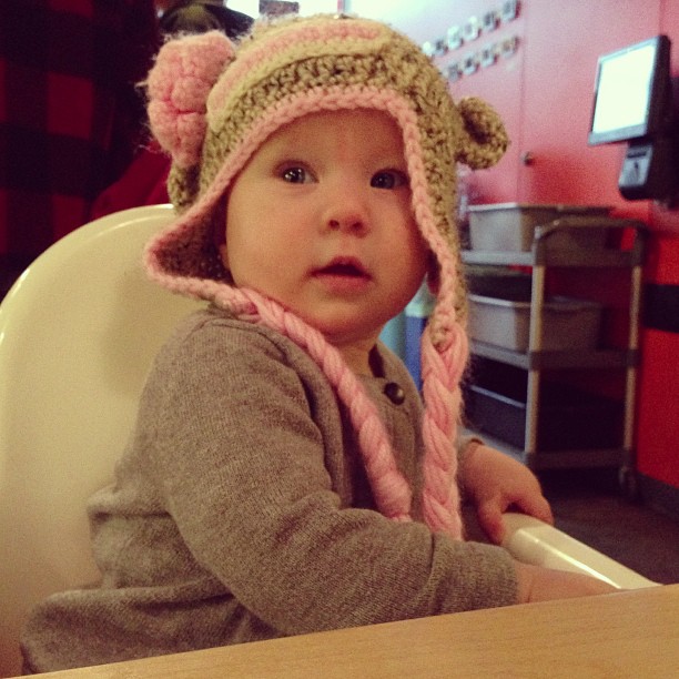a baby sits in a high chair wearing a cute hat