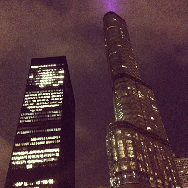 two large skyscrs in the city one is lit purple