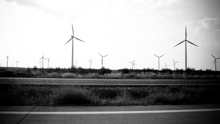 several wind turbines are seen behind an empty street