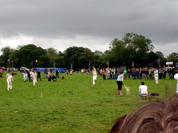 people in white clothing walking on grass with a large group of trees