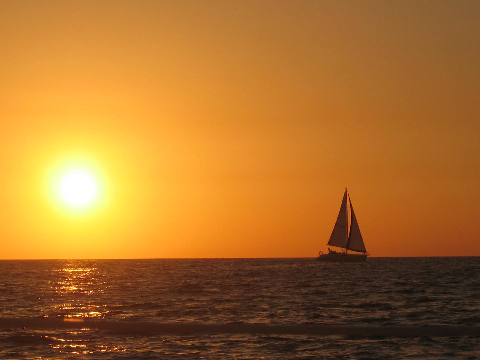 the sun rising over a sailboat in the water