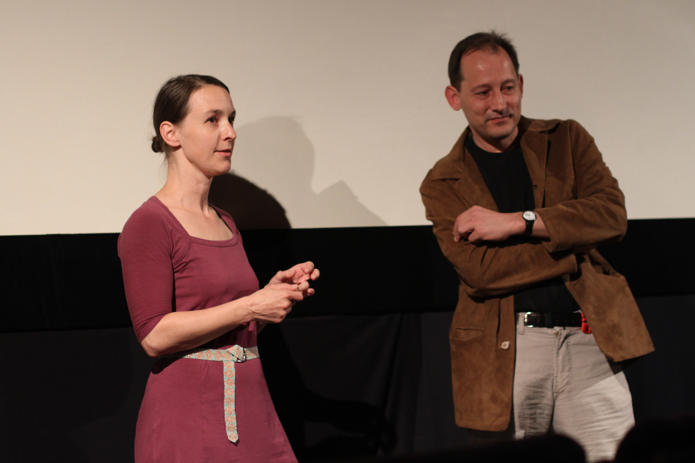 two people speaking and standing in front of a projection screen
