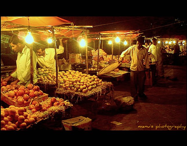two men looking at a fruit stand at night
