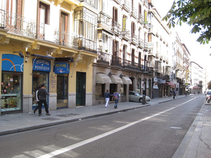 people walk past shops in a city, including a couple walking down the street