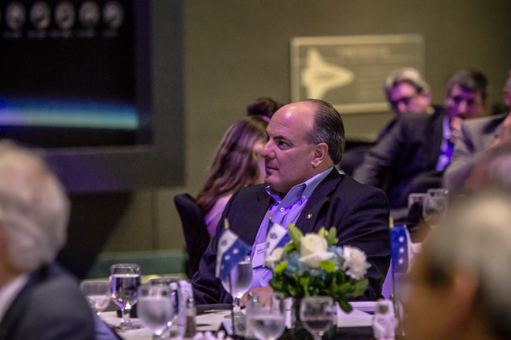 two men sitting at a table with people eating and talking