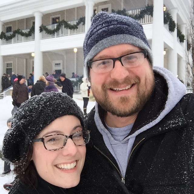 a smiling couple standing together in front of a white house