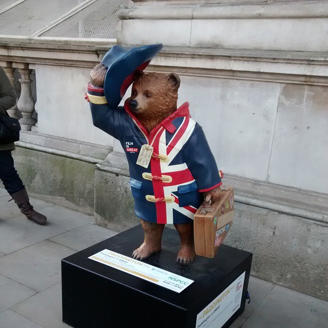 a statue of a bear wearing an outfit and holding a luggage bag