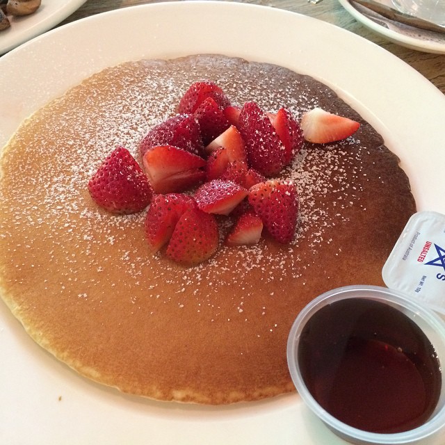 a table holding a plate of pancakes with syrup and strawberries