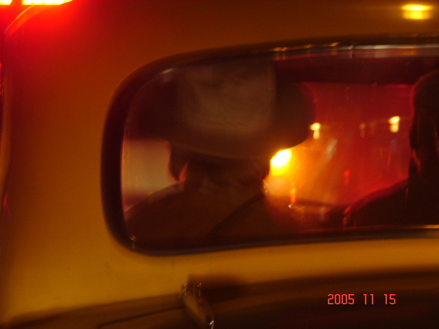 the rear view mirror on a car reflects a man wearing a cowboy hat