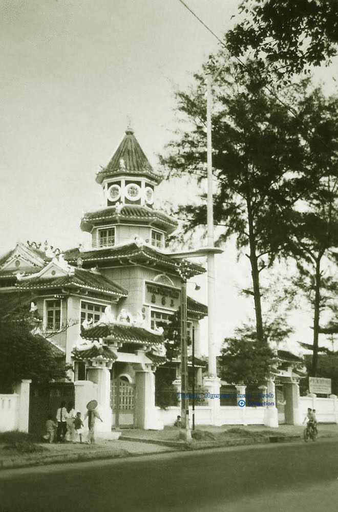 an old po shows a white building with trees and a man riding on a bike