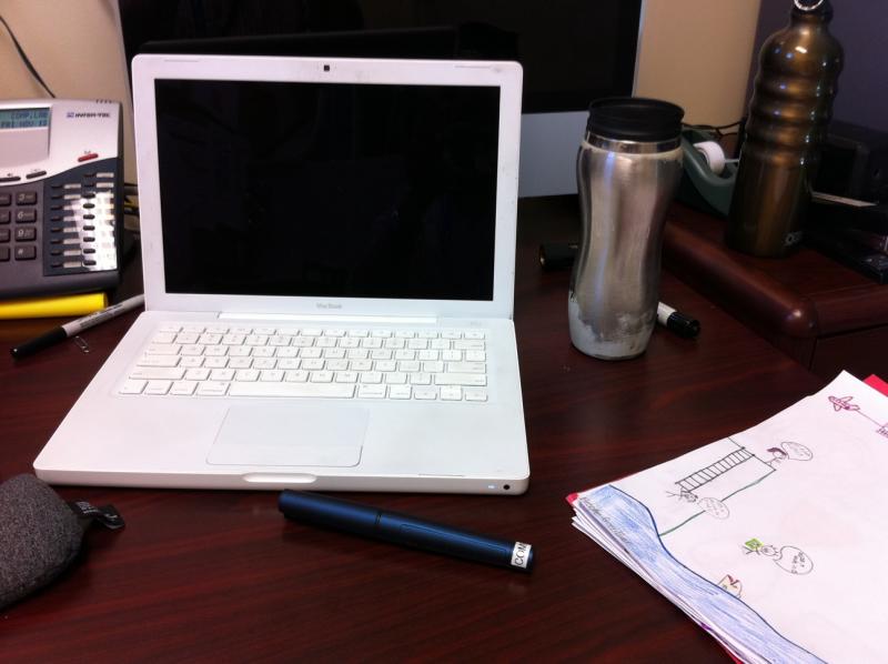 a table with a lap top and some pen and a cup