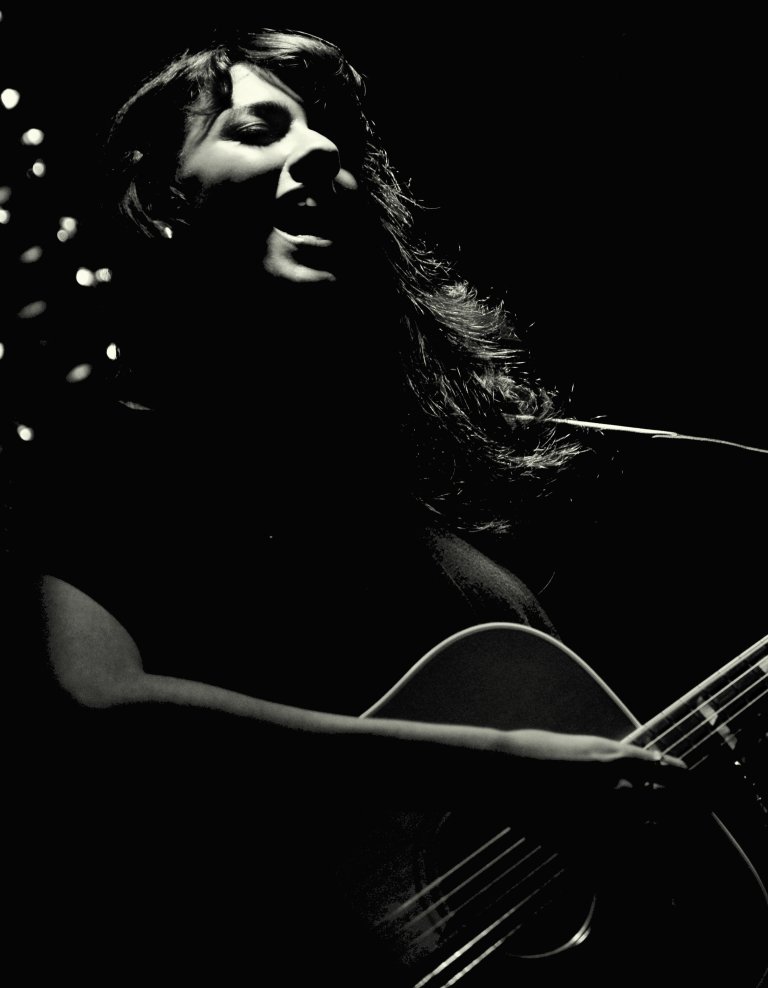 black and white pograph of woman holding guitar at night