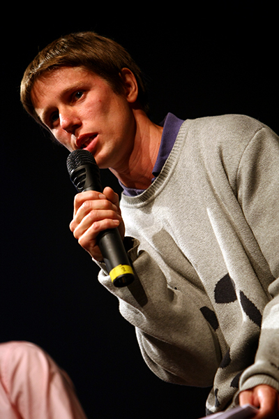 a young man in a gray sweater holds a microphone in one hand