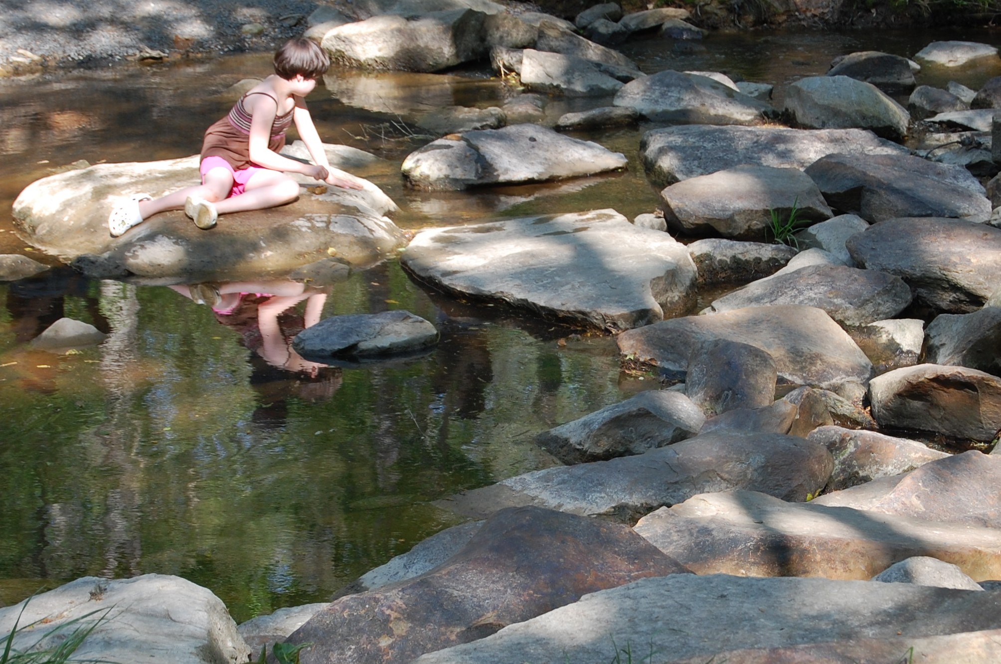 a woman sits on a rock in a creek