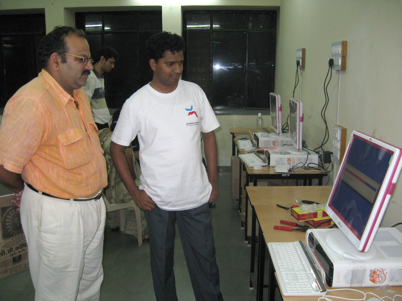 two men stand next to a desk with a laptop on it