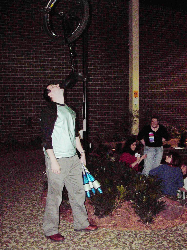 people sitting and standing around near the ground while a man holds a camera up to a light post