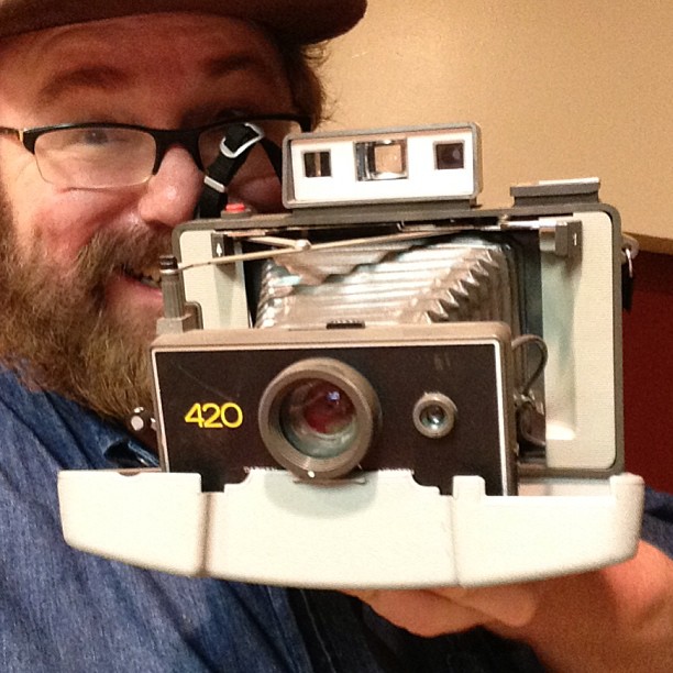 a man holding up an old - fashioned camera while wearing glasses and a fedora