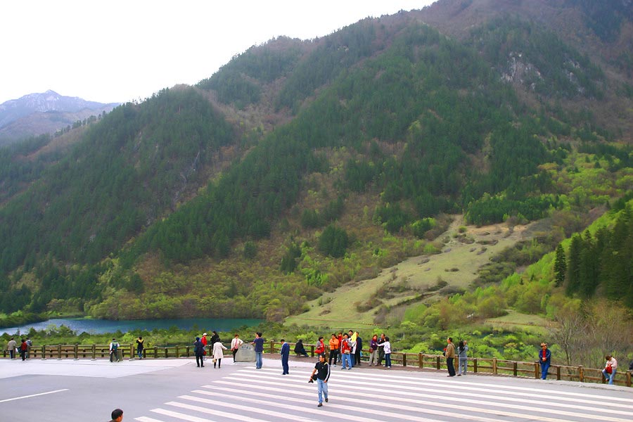 a crowd of people walking across a wooden walkway next to mountains