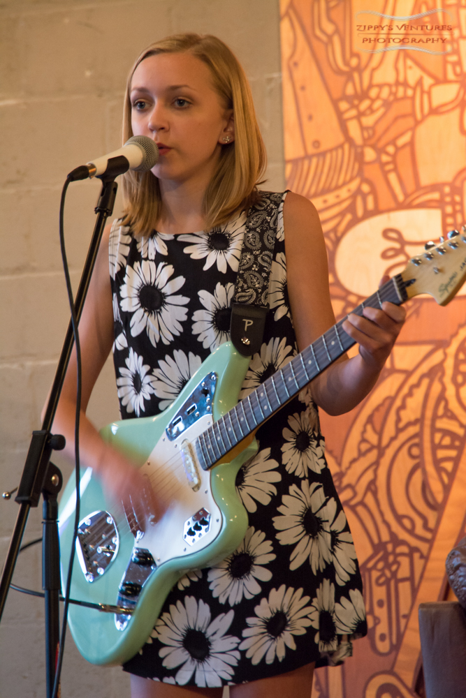 a woman standing in front of a microphone playing an electric guitar