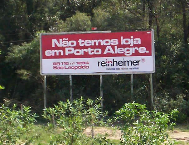 a red and white sign reads nao temos, loia em porto alegre, next to some trees