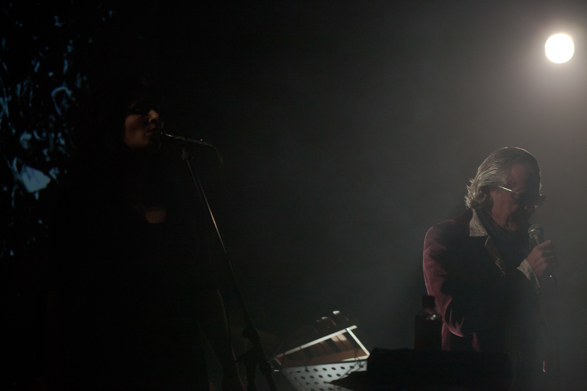 a man holding a microphone standing on stage next to a piano