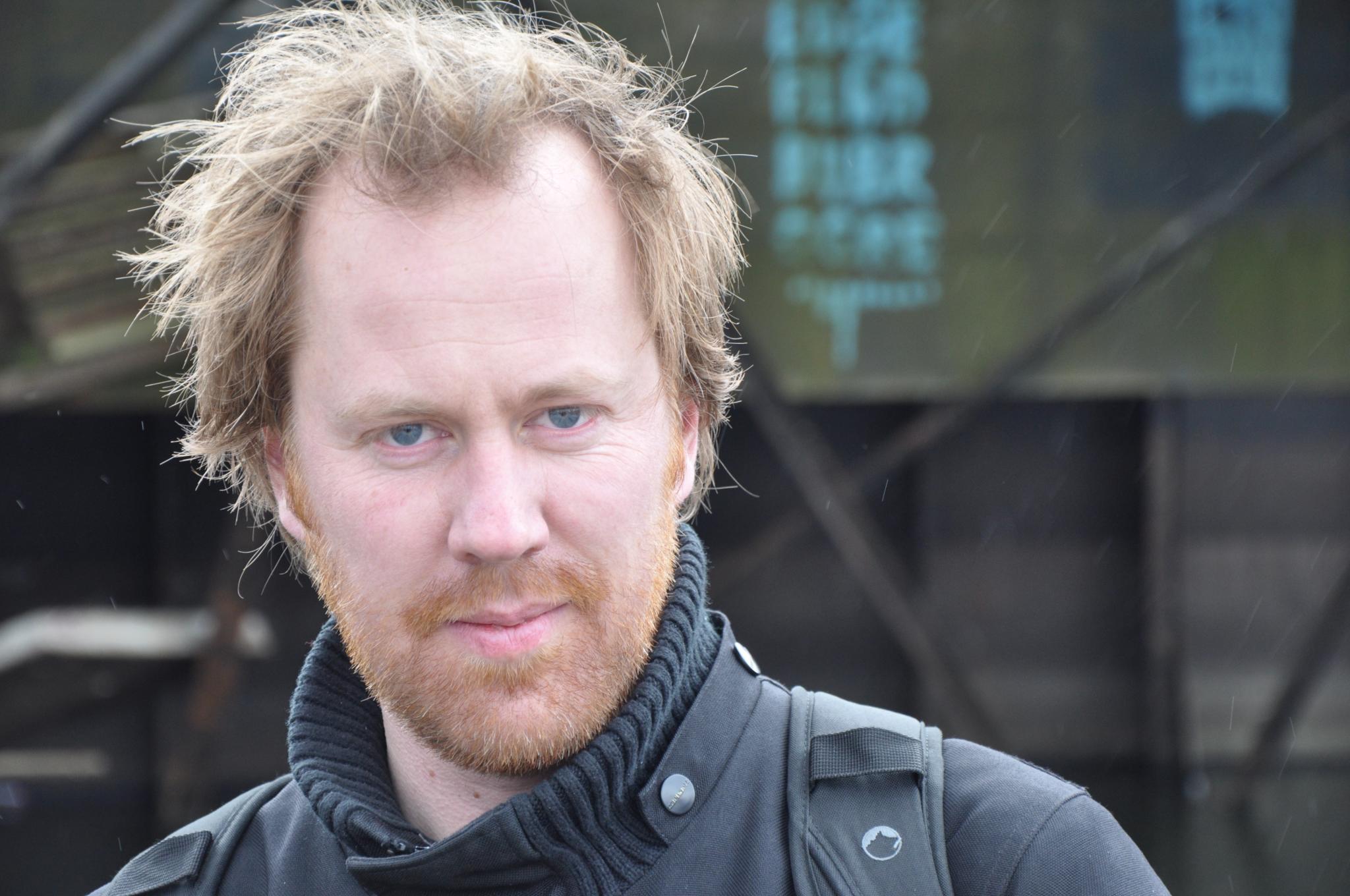 man with thick hair and scarf stares at the camera