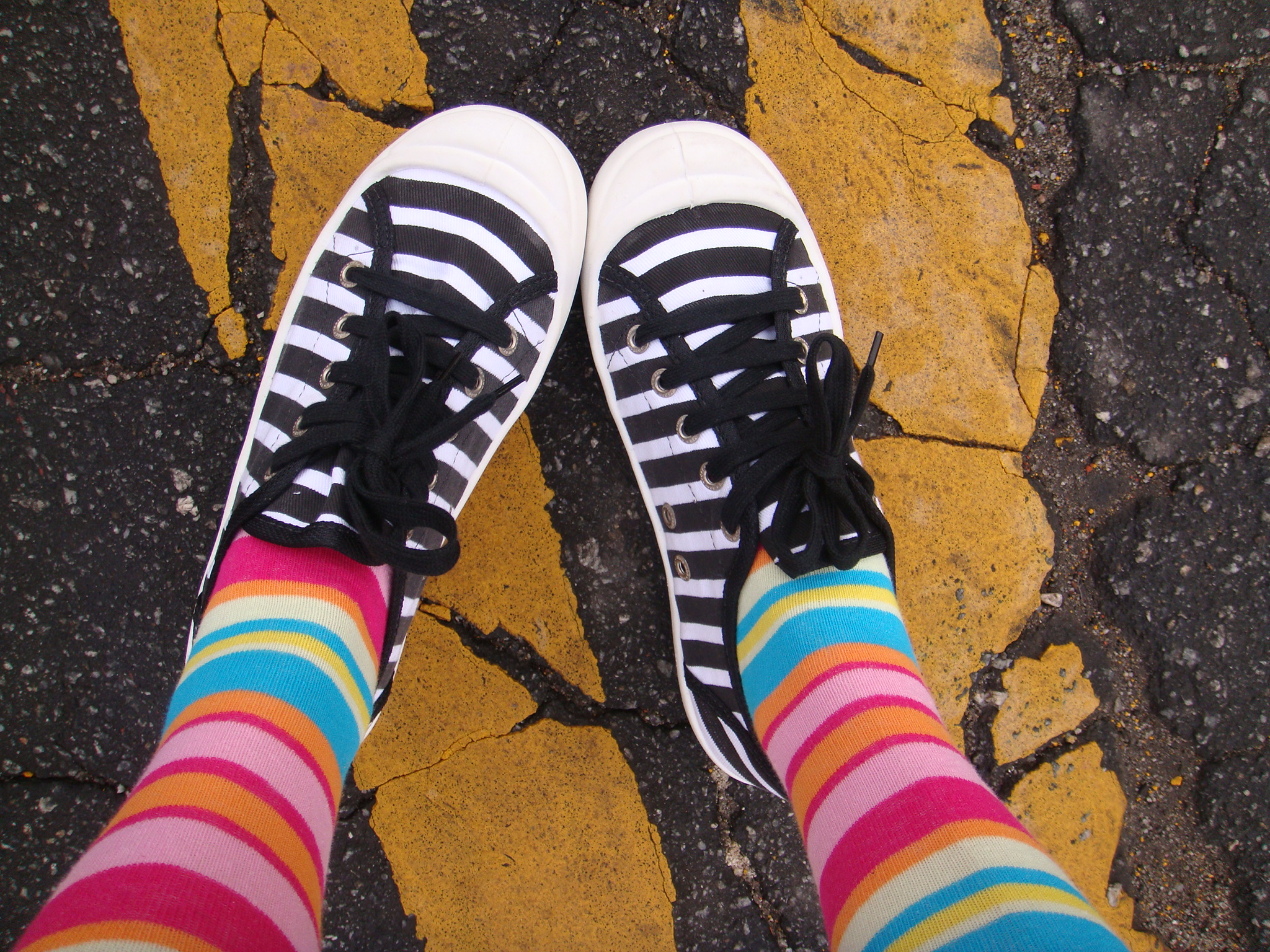 two legs in colorful socks standing on yellow striped sidewalk